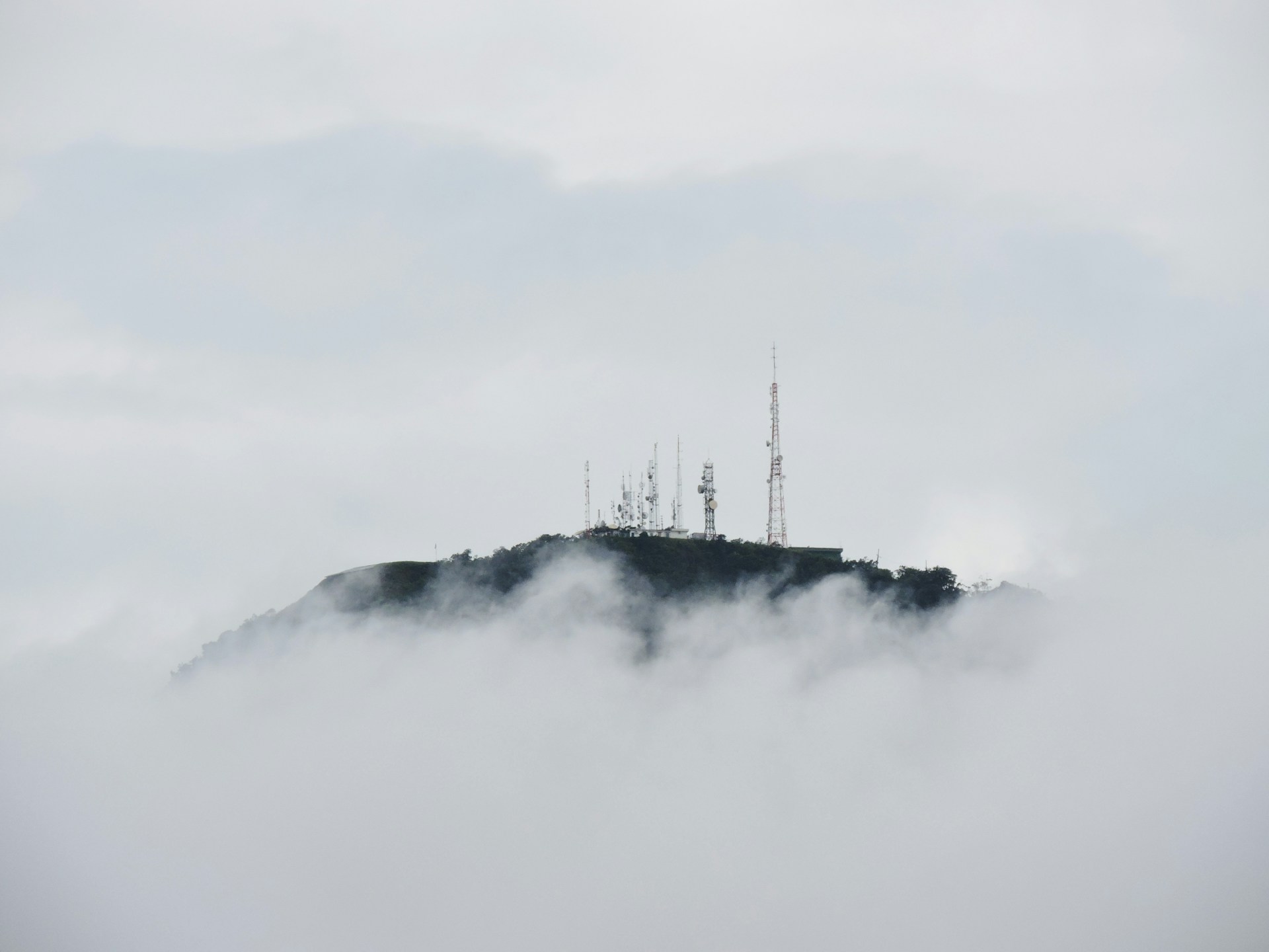Communications towers atop a mountain peek out above billowing white clouds