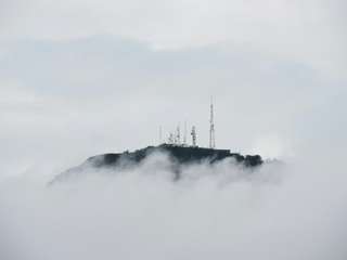 Communications towers atop a mountain peek out above billowing white clouds